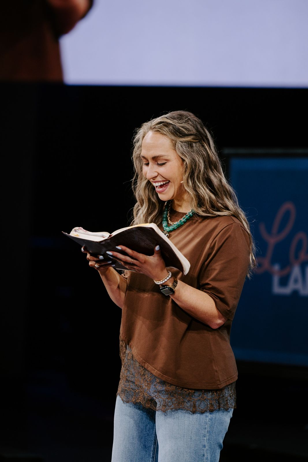Kate Downing laughing as she reads from her Bible on stage