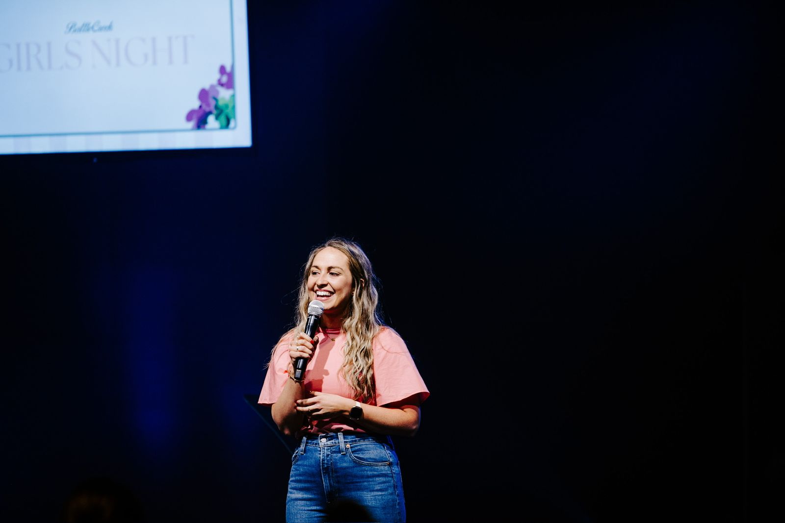 Kate Downing in a pink shirt speaking into a microphone on stage